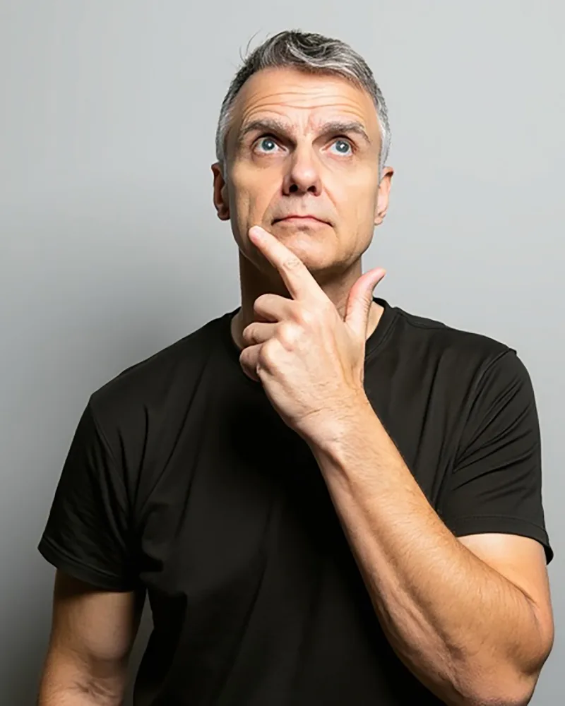 Bart Cleveland, in a black T-shirt against a grey backdrop, looking up with a finger resting on his chin.